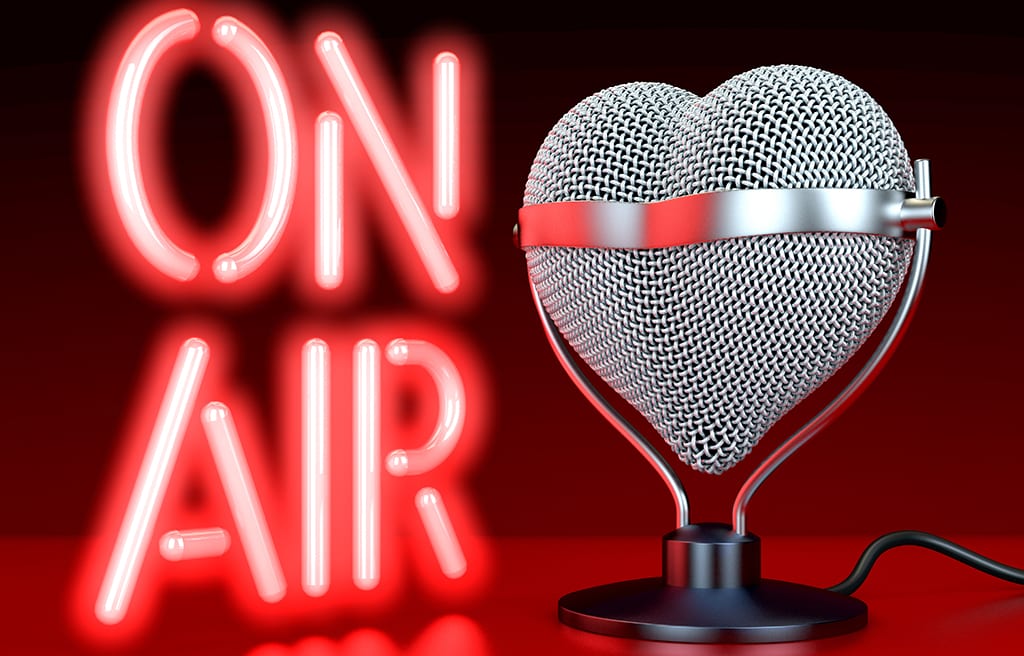 Heart shaped microphones on reflecting, red surface in front of, lateral to neon sign