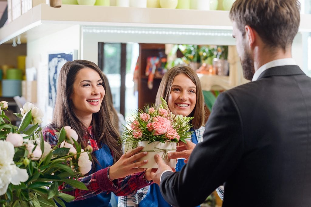 Smiling girls giving a bouquet to the man. Two sisters doing small family business, selling flowers at their shop